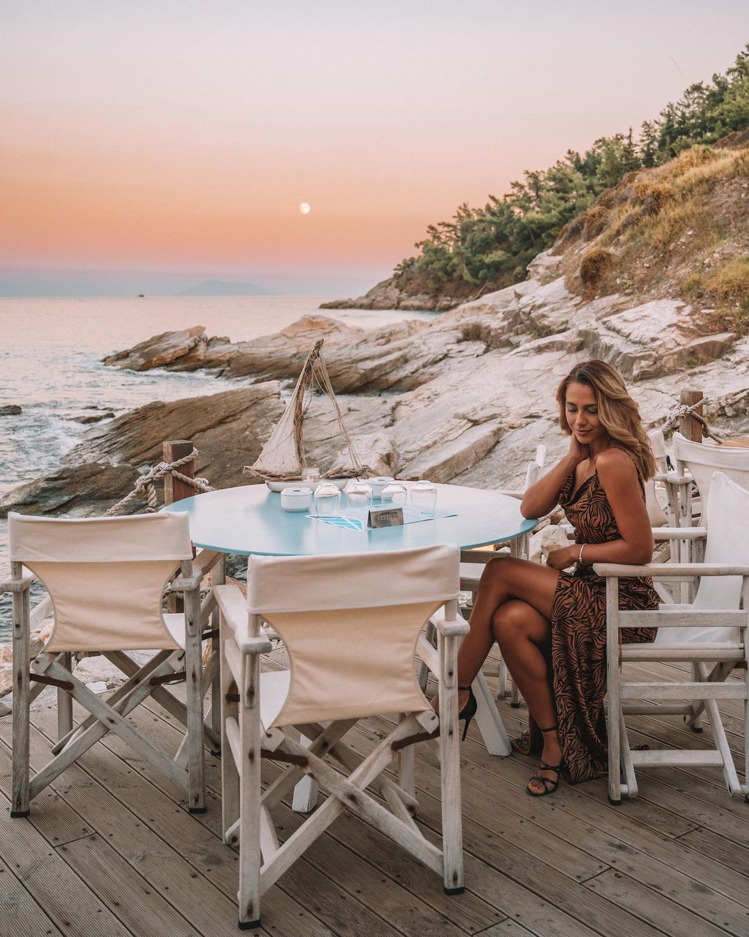 Girl sitting at a table while the sun is setting down at Thassos Karnagio Bar