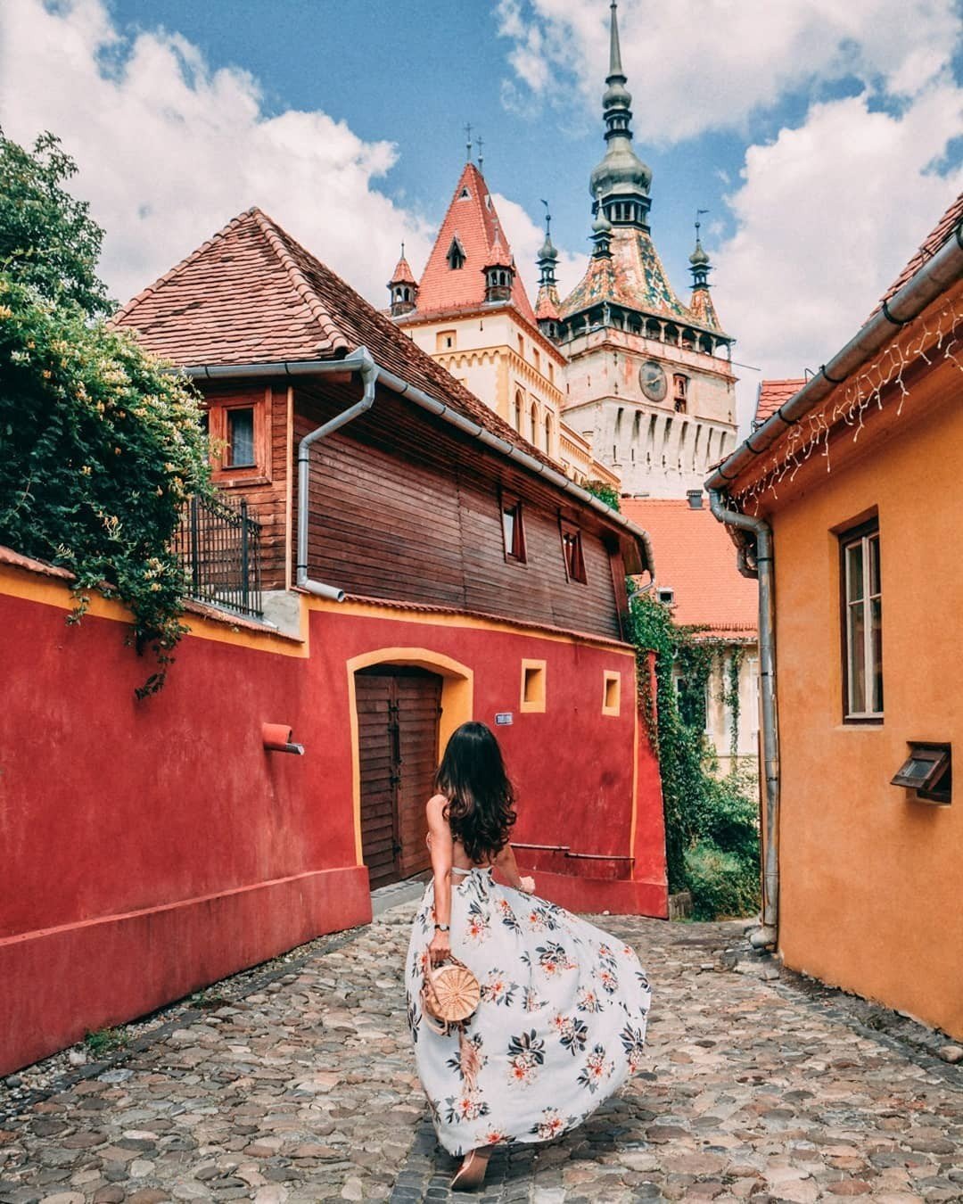 Girl with a white dress and summer flowers at the entrance to the colorful and charming citadel of Sighisoara